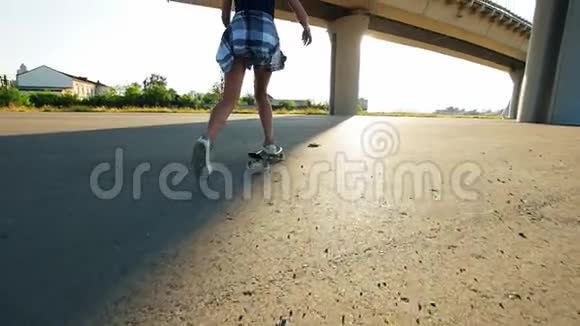 美丽的女孩骑着滑板在桥下的太阳在腿的框架视频的预览图