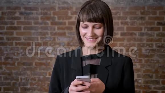 年轻漂亮的女人在电话里谈笑风生站在砖墙附近迷人的女人剪短了头发视频的预览图