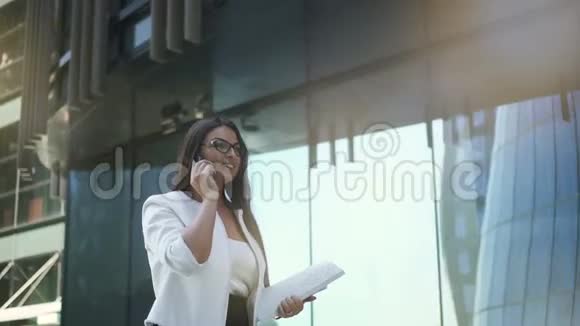 年轻有魅力的女商人正在打电话走在办公楼外面视频的预览图