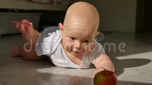 六个月大的婴儿躺在地板上伸手要一个红苹果孩子学会了爬行视频的预览图