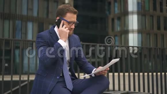 一位穿着蓝色西装的自信商人在电话中谈论他手上的文件视频的预览图