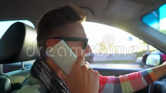 年轻人开着车在户外的日落天空用手机说话微笑和欢笑的司机特写视频的预览图