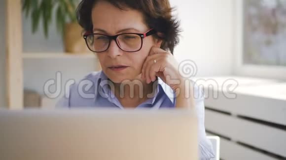 家中坐在笔记本电脑屏幕前的老年商务女士的肖像视频的预览图