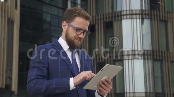 年轻自信的商人正在公司建设的背景上使用平板电脑视频的预览图
