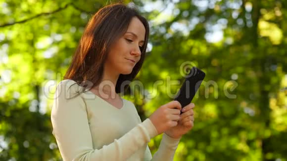 带着智能手机的女人环顾四周模糊的自然背景视频的预览图