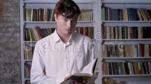 严肃的黑发男人正在看书在镜头前看在后台看图书馆视频的预览图