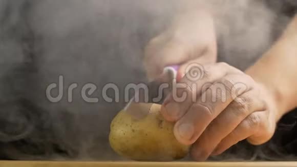 一个人用刀切一块新鲜的土豆里面有烟雾和蒸发特写黑色背景慢莫素食视频的预览图