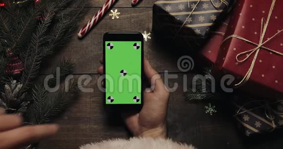 圣诞老人的手在黑色智能手机上用绿色屏幕敲击页面铬钥匙上景垂直位置视频的预览图