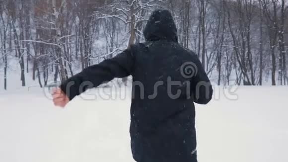 穿着黑色引擎盖和时髦靴子的人在下雪的中央公园跑步下雪了慢动作背面视频的预览图