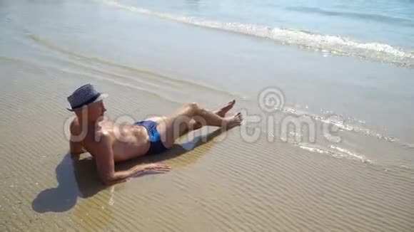 夏季生活方式高清视频美丽的年轻晒黑男子戴帽子享受生活坐在海滩上旅行的时间视频的预览图