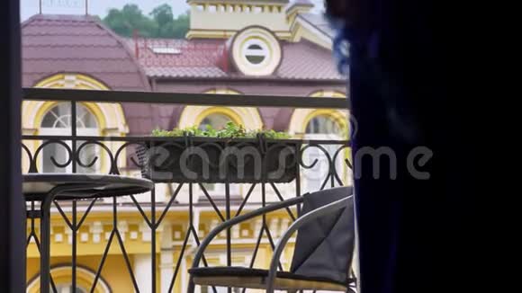 年轻的穆斯林妇女戴着头巾在阳台上坐在椅子上放松和眺望视频的预览图