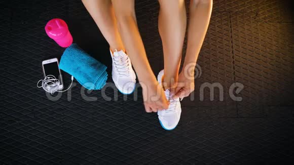 一位身材匀称的女士坐在健身房的地板上系鞋带运动鞋视频的预览图