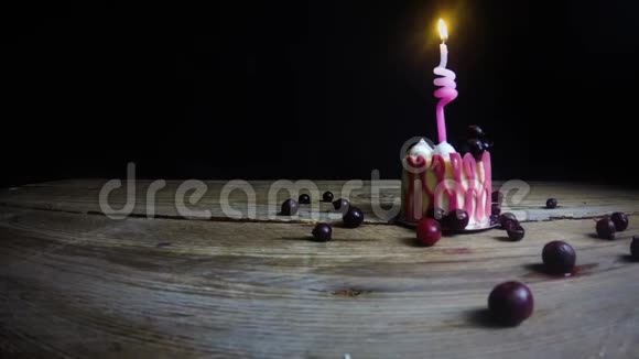 一支燃烧着的蜡烛在一张老式木桌上的一个喜庆的粉红色纸杯蛋糕上燃烧着手拿起蜡烛在黑色的视频的预览图