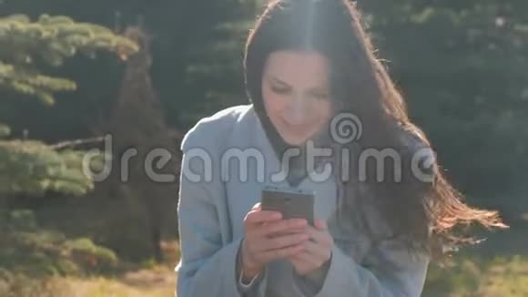 年轻漂亮的黑发女人坐在春天公园的草地上用手机读一条信息视频的预览图