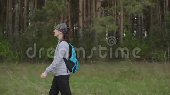 徒步旅行中背着背包的年轻女子在森林的背景下沿着小径散步视频的预览图
