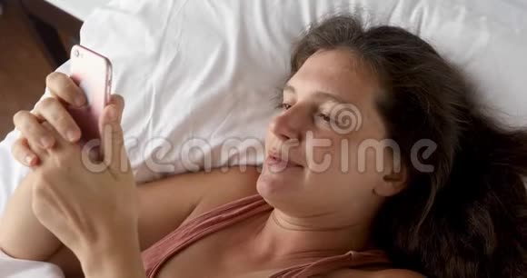 漂亮的女人躺着看电话视频的预览图