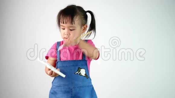 可爱的亚洲小女孩拿着画笔在白色背景上孤立地作画的肖像视频的预览图
