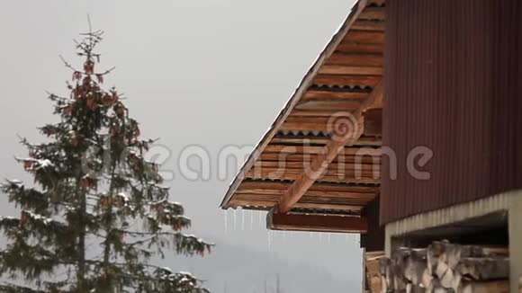 林中一座木屋的屋顶上挂着的冰柱树上有云杉树顶背景是圆锥形和小山视频的预览图