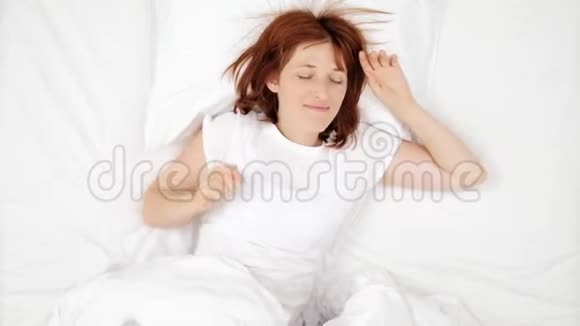 美丽的年轻红发女人睡在白色的床上早上好黎明清晨升起女人在睡觉女孩视频的预览图