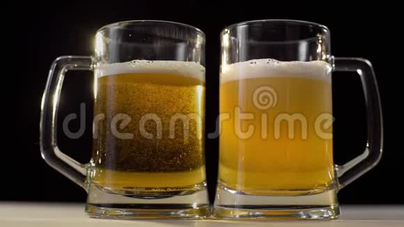 两个啤酒杯在黑色背景上倒入泡沫金色的淡啤酒和朋友一起喝啤酒两个人喝饮料视频的预览图