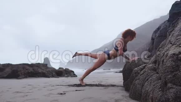 女运动员在一个美丽的海滩上训练时从岩石上进行挤压视频的预览图