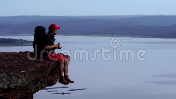 一个背着背包的人用照相机在悬崖边上的岩石山上拍照视频的预览图