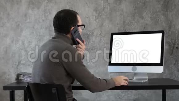 男人在办公室打电话看电脑屏幕白色显示器视频的预览图