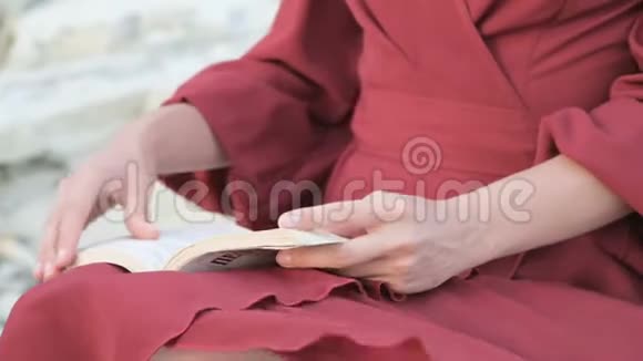在海边的一块大石头上一个穿着红色鲜艳连衣裙戴着草帽的漂亮白种人女孩紧紧地抓住了她的双手视频的预览图