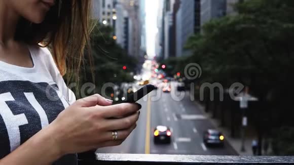 近距离观看年轻女性使用智能手机站在桥上附近的交通道路在纽约美国视频的预览图
