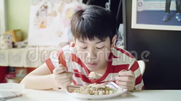 可爱的泰国男孩在客厅的白色桌子上吃炒饭视频的预览图