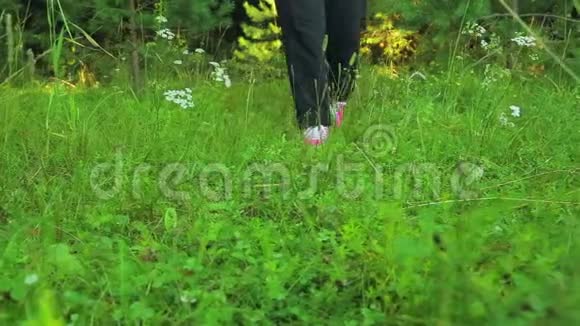 女人穿着运动鞋腿穿过森林或公园里的草地前面的风景视频的预览图