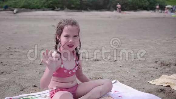 小女孩坐在沙滩上炎炎夏日挥手微笑视频的预览图