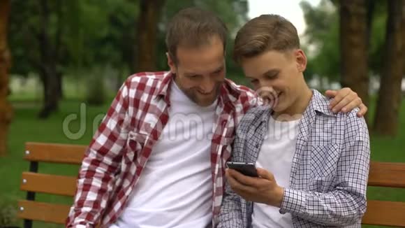 男青少年和爸爸在智能手机上看有趣的视频笑着笑着视频的预览图