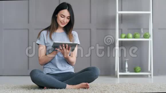 年轻快乐的女人坐在地板上在家里使用平板电脑视频的预览图