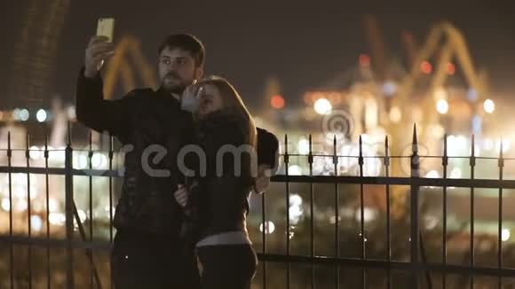 年轻的幸福夫妇在智能手机上的相机上拍摄自拍照片港口夜间灯光视频的预览图