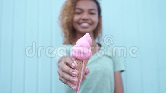 微笑着的黑人女孩在蓝墙背景下缓慢地吃粉色融化的冰淇淋视频的预览图