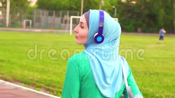 迷人的穆斯林女孩戴着头巾在体育场周围走来走去对着镜头微笑慢悠悠视频的预览图