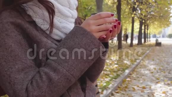 秋天公园里穿着灰色外套的年轻的南方黑发女人正在喝热水杯中的热饮料视频的预览图