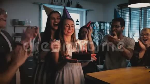 快乐的欧洲女孩拿着生日蛋糕许愿吹着多民族朋友在欢乐的聚会上唱着慢动作视频的预览图