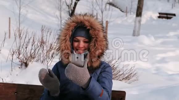 年轻快乐的美女打电话视频聊天在冬天的公园里在下雪的日子里在城市里下雪了视频的预览图