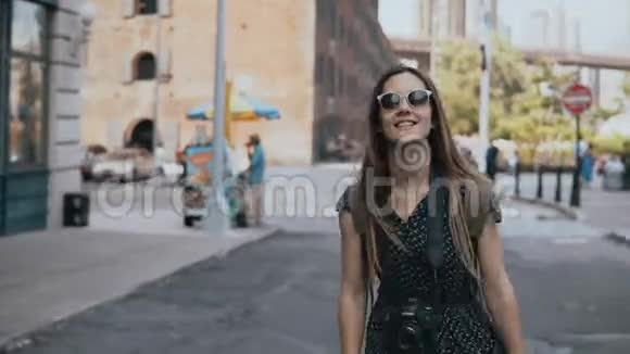 镜头跟随嬉戏兴奋的欧洲旅游女孩戴着太阳镜背包举手和微笑快乐4K视频的预览图