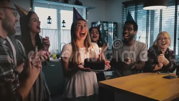 快乐兴奋的白种人女孩拿着生日蛋糕多民族的朋友在有趣的聚会上唱着欢快的歌慢动作视频的预览图