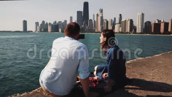 在美国芝加哥密歇根湖畔野餐的年轻夫妇男人在智能手机拍照视频的预览图