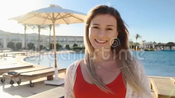 微笑的少女看着镜头阳光明媚的天气蓝色游泳池附近穿红色泳衣的美女视频的预览图