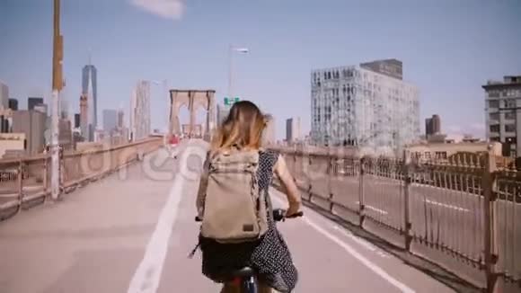 在纽约布鲁克林大桥的一条美丽的自行车道上一位黑发随风飘动的后景妇女骑着自行车视频的预览图