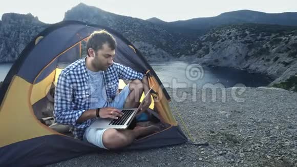 自由职业者使用笔记本电脑在海滩露营帐篷工作从事新启动项目的自由职业者视频的预览图