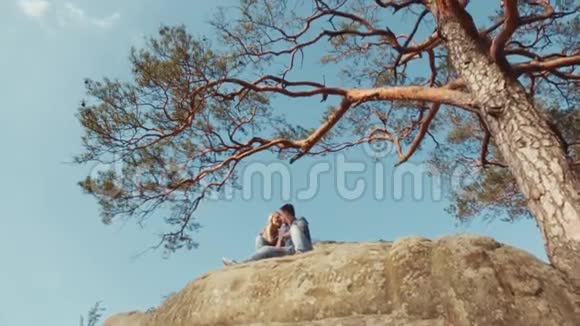 一对穿着休闲装的年轻夫妇在岩石山上坐着聊天在地板上观看高绿的树视频的预览图