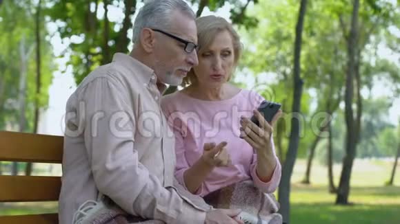 老人帮助老伴使用智能手机快乐的老夫妇一起在公园里视频的预览图
