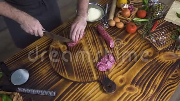 在新鲜蔬菜背景下男人在木桌上切香肠沙拉米厨师把香肠切成薄片视频的预览图