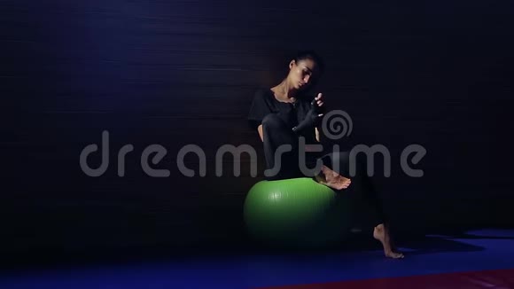 可爱的女人黑发运动员坐在健身球上在训练前热身视频的预览图